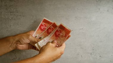 İsrail 'de mali yönetim ve para yönetimi gösteren somut bir arkaplan karşısında İsrail şekeli banknotları tutan eller
