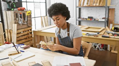 Afrikalı bir kadın marangozluk atölyesinde marangozluk aletleriyle çevrili Güney Afrikalı randaları sayıyor..