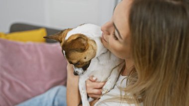 Sarışın kadın sevgi dolu bir şekilde küçük bir köpeği evde tutuyor ve sevgi dolu bir hayvan sahibi ilişkisi sergiliyor..