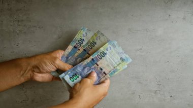 Hands holding south african rands against a concrete background, showcasing money, currency, and finance. clipart