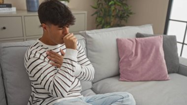 Modern bir oturma odasında rahat bir koltukta oturan yakışıklı İspanyol bir adam endişeli ve düşünceli görünüyor, evde çizgili bir gömlek giyiyor..