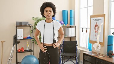 Kıvırcık saçlı Afrikalı Amerikalı bir kadın spor salonunda elinde ip tutarak duruyor..