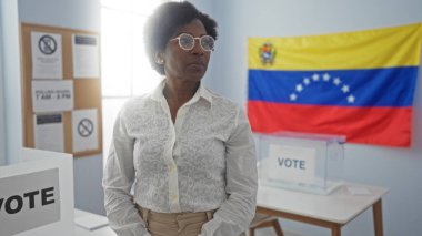 Kıvırcık saçlı Afrikalı Amerikalı bir kadın kapalı bir seçim odasında Venezuela bayrağının önünde duruyor ve oy verme sürecini vurguluyor..