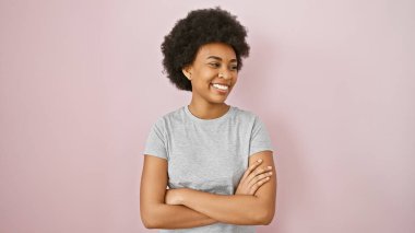 Kıvırcık saçlı, pembe duvarın karşısında gülümseyen kendine güvenen Afro-Amerikan kadın.