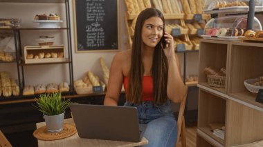 Ekmek, hamur işleri ve tezgahla çevrili bir şekilde fırında çalışırken telefonla konuşan bir kadın.