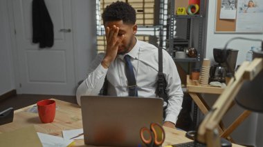 Karakolda kahve ve dizüstü bilgisayarlı stresli bir Afro-Amerikan dedektifi..