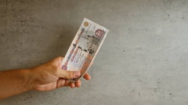 Elle tutulan Mısır sterlini beton bir arka planda, ayrıntılı para birimi özellikleri sergiliyor.