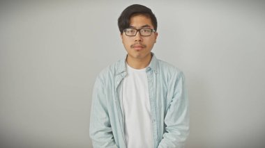 Sıradan giyinmiş yakışıklı genç Asyalı beyaz bir arka plana karşı güvenle poz veriyor..