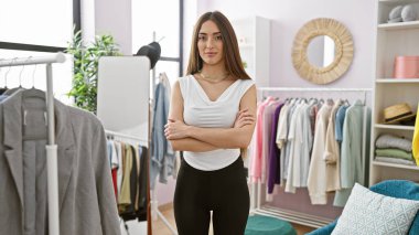 Parlak bir giyim mağazasında kollarını kavuşturmuş kendine güvenen bir kadın.