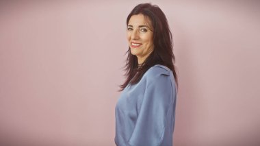 Dost canlısı, orta yaşlı İspanyol bir kadın, mahrem bir pembe arka plana karşı güvenle poz veriyor, olgunluk gösteriyor..
