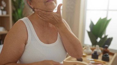 Spa salonunda boynundaki kremi süren olgun bir kadın, bir sağlık merkezinde cilt bakımını gösteriyor..