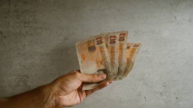 Servet ve finansmanı vurgulayarak, somut bir zemine karşı beş adet 5 pound 'luk İngiliz banknotunu elinde tutmak