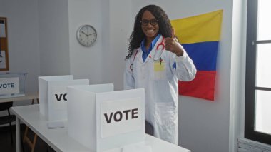 Genç Afrikalı Amerikalı bir kadın Venezuela 'da bir üniversite odasında oy veriyor, laboratuvar önlüğü giyiyor ve baş parmağıyla gülümsüyor..