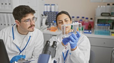 A man and woman in lab coats examine test tubes together in a scientific laboratory indoor setting. clipart