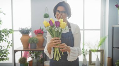 Gülümseyen olgun kadın çiçekçi elinde çiçekle parlak bir çiçekçi dükkanında