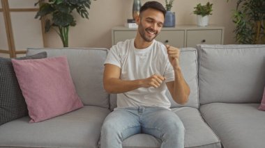 Evdeki oturma odasındaki kanepede dans eden genç İspanyol adam mutlu ve rahat görünüyor.