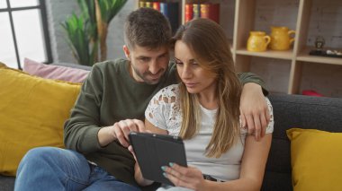 Sevecen bir çift modern bir oturma odasında bir tabletle içli dışlı oluyor. Teknoloji, samimiyet ve ev konforu tasvir ediyorlar..