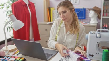 Odaklanmış genç bir kadın, iyi donanımlı bir terzi dükkanında kumaş örneklerini inceleyerek moda tasarımındaki yaratıcılığı ön plana çıkarıyor..