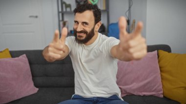 Orta yaşlı, sakallı bir adam. Günlük giysiler içinde. Kapalı bir koltukta renkli yastıklarla oturuyor..