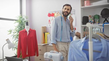 Neşeli sakallı bir terzi. Parlak bir atölyede mezurası var. Etrafı giysi ve dikiş malzemeleriyle çevrili..