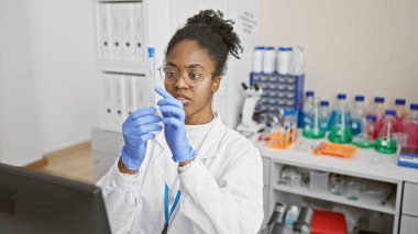 İyi donanımlı bir laboratuarda test tüpünü analiz eden odaklanmış Afro-Amerikan kadın bilim adamı..