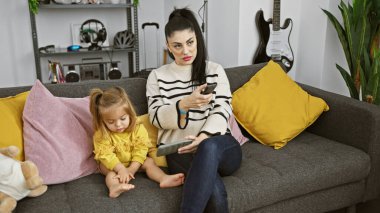 Bir kadın ve bir kız modern bir oturma odasında kanepede otururken teknolojiyle meşgul oluyorlar..