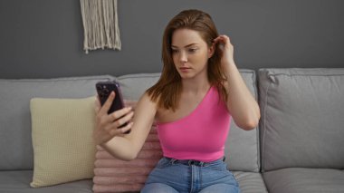 Modern bir oturma odasında telefona bakarken saçları düzelten bir kadın.