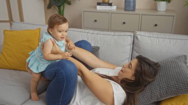 Modern bir oturma odasındaki rahat bir kanepede kızıyla oynayan bir kadın bir aile evinde sevgi ve neşe anı yakalıyor.