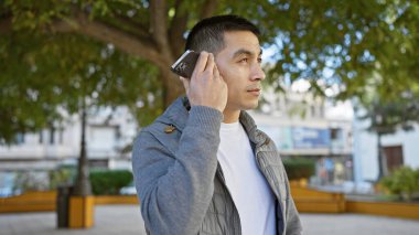 Sunny Park ortamında akıllı telefon kullanan yakışıklı adam modern şehir yaşam tarzını gösteriyor..