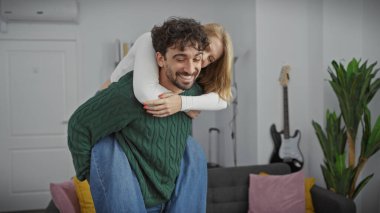 A joyful woman embracing a laughing man from behind in a cozy living room with modern decor. clipart