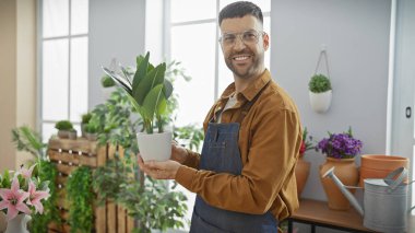 Smiling man holding plant in sunlit flower shop, conveying a sense of freshness and retail business. clipart