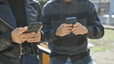 Güneşli bir şehir sokağında akıllı telefonlarına sarılmış genç bir çiftin yakın çekimi..