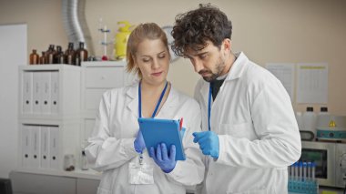 Laboratuvar önlüklü bir adam ve kadın, iyi donanımlı bir laboratuardaki tabletteki verileri gözden geçiriyorlar..