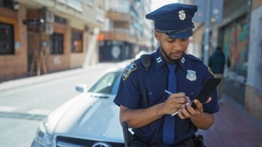 Afro-Amerikan polisi arka planda devriye arabasıyla şehir dışında ceza yazıyor..