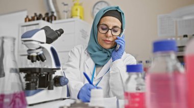 Laboratuvarda tesettürlü İspanyol kadın bilim adamı telefonda konuşuyor.