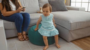 Akıllı telefon saatleri kullanan mavi elbiseli kız rahat oturma odasında puf üzerinde oturuyor..