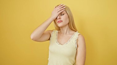 Açık renk bluzlu dalgın bir sarışın kadın alnına sarı bir zemine dokunuyor. Bu da tefekkür veya baş ağrısı olduğunu gösteriyor..