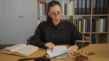 Çekici İspanyol esmer kadın mahkeme salonundaki iş yerinde adalet ve hukuk kitaplarının tokmaklarıyla doküman okuyan hâkim.