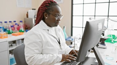 African american woman with braids working on a computer in a laboratory setting clipart