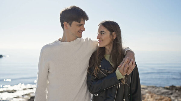 Любящая пара обнимается у моря, с безмятежным океанским фоном, освещающим их случайный момент на открытом воздухе.