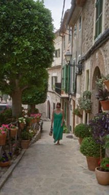 Valldemossa 'da, Mallorca' da, İspanya 'da, yemyeşil, canlı çiçekler ve büyüleyici eski binalarla çevrili güzel taş bir caddede yürüyen bir kadın..