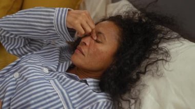 Gündüz vakti çizgili pijama giyen ve yatak odasında acı çeken bir kadın yatakta yatıyor.