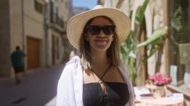 Güneş gözlüklü ve şapkalı genç bir kadın Fornalutx, Mallorca, İspanya 'da güneşli bir günün tadını çıkarıyor.