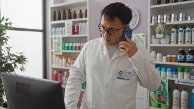 Genç Asyalı bir adam bir eczanede çalışıyor, akıllı bir telefonla konuşuyor ve Çin 'de çeşitli ilaç ve kimyasal ürünlerle çevrili bir bilgisayar ekranına bakıyor..