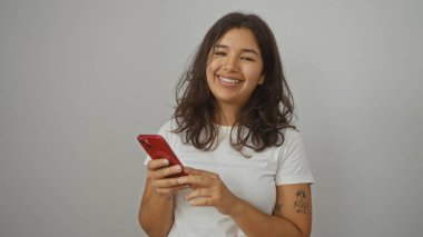 Beyaz bir arka planda izole edilmiş kırmızı bir akıllı telefon kullanarak gülümseyen genç, çekici İspanyol kadın..