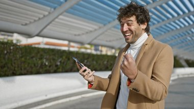 Sakallı, neşeli, genç bir İspanyol. Gülüyor ve akıllı telefonunu şehrin dışında tutuyor..