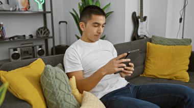 Modern bir oturma odasında şık dekorlu bir tablet kullanan genç bir İspanyol..