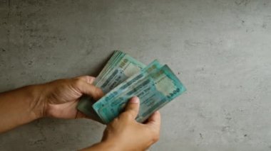 Bangladeshi Taka 'yı tutan adam somut bir arkaplana karşı notlar tutuyor, yakın planda para birimini parmak ve ellerle vurguluyor.