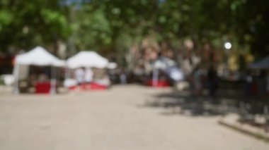 Mallorca 'da açık hava pazarı. Bulanık beyaz çadırlar ve arka planda yeşil ağaçların altında insanlar var.