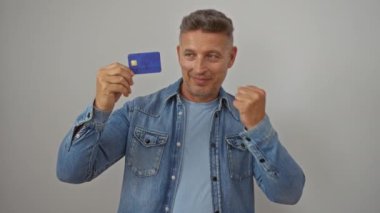 Kot gömlekli orta yaşlı adam, beyaz arka planda kredi kartı taşıyarak kutlama yapıyor.